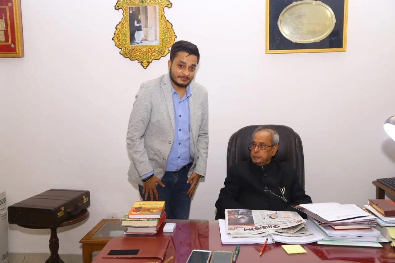 Nitish Jindal standing beside seated Pranab Mukherjee across a desk.
