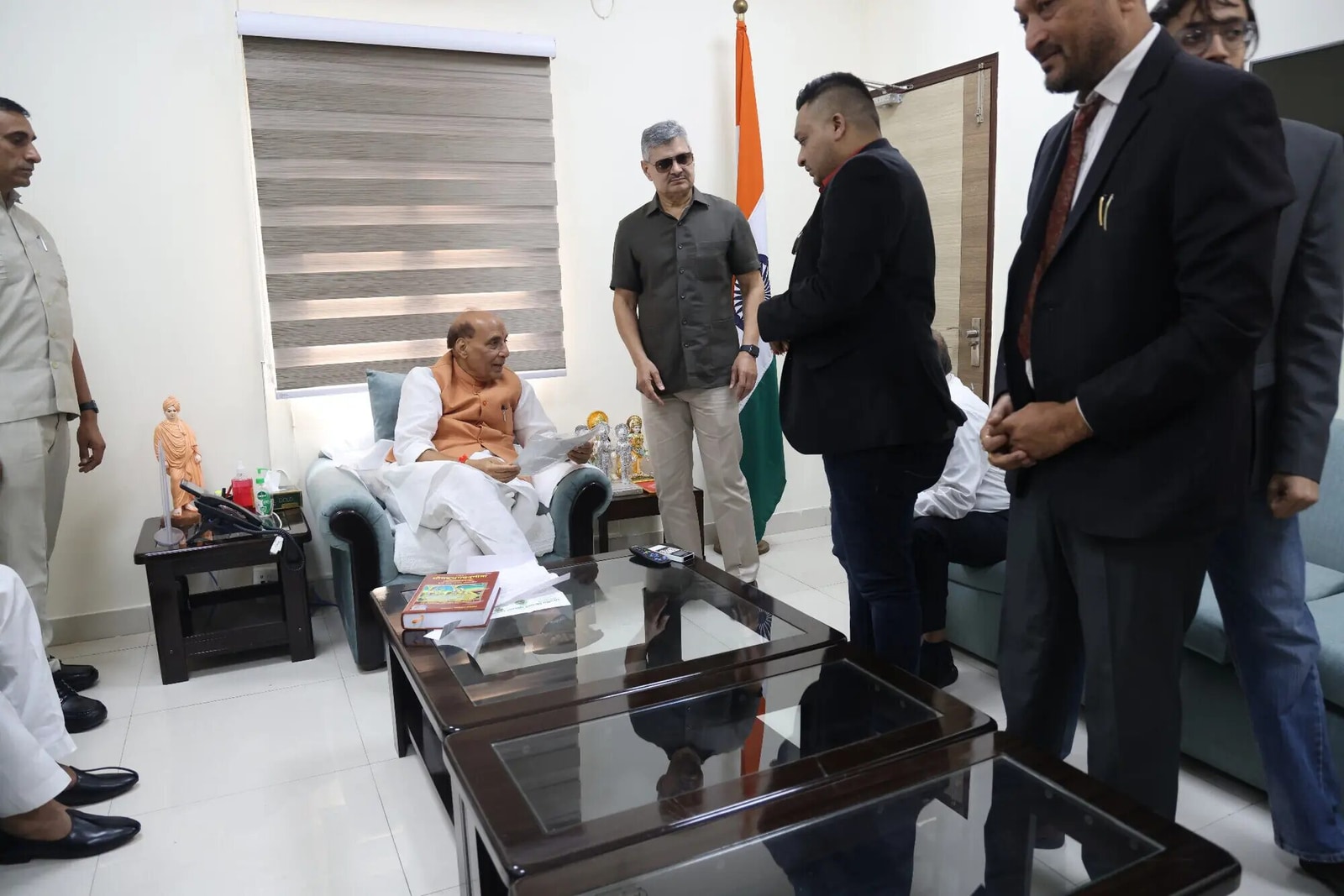 Nitish Jindal standing near seated Rajnath Singh in a group meeting-room scene.